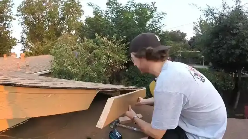 Roofer replacing a damaged fascia board along the edge of a residential roof.